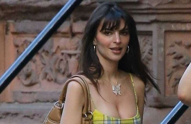 Emily Ratajkowski adjusts her yellow micro mini dress with blushing smile