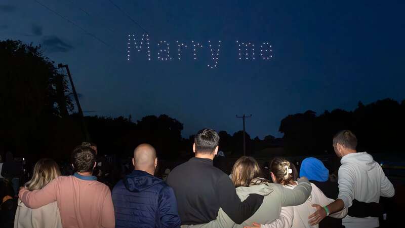 Drones spell out the words "Marry me" as Rhys Whelan (forth left) proposes to Megan Greenwood (fifth left) (Image: PA)