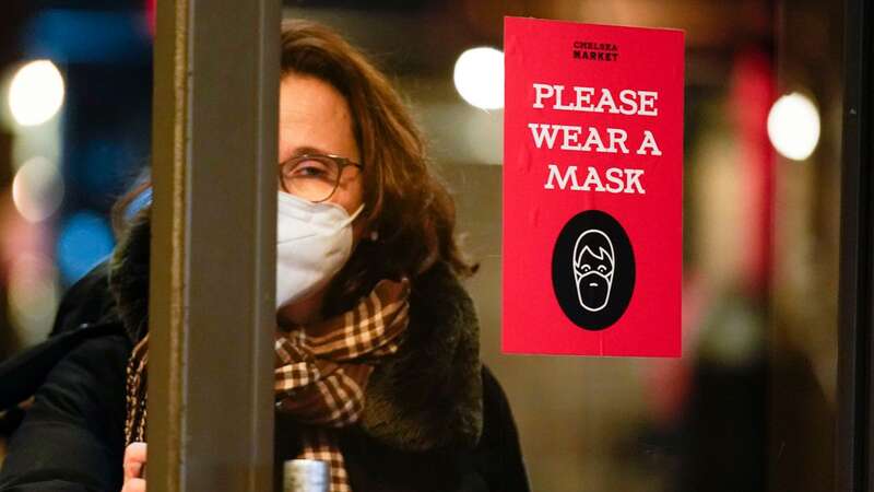 A woman walks through a door with a sign asking shoppers to wear masks, in New York, Feb. 9, 2022. (Image: AP)