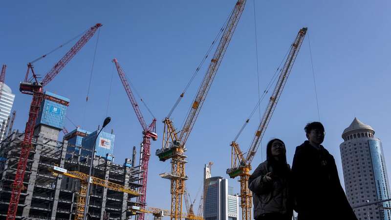 A young couple walk by a construction site near office buildings in the Central Business District in Beijing (Image: Copyright 2024 The Associated Press. All rights reserved)