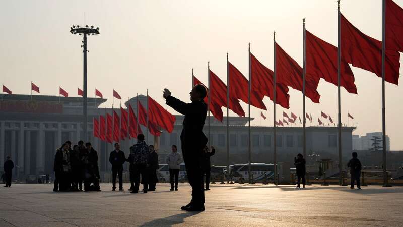 A man takes photos near red flags on Tiananmen Square before the closing session of the Chinese People