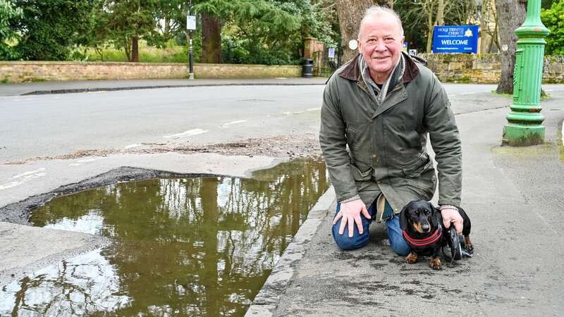 Local resident Matt Beacham, 57, with his sausage dog Richmond next to the huge pothole (Image: SWNS)