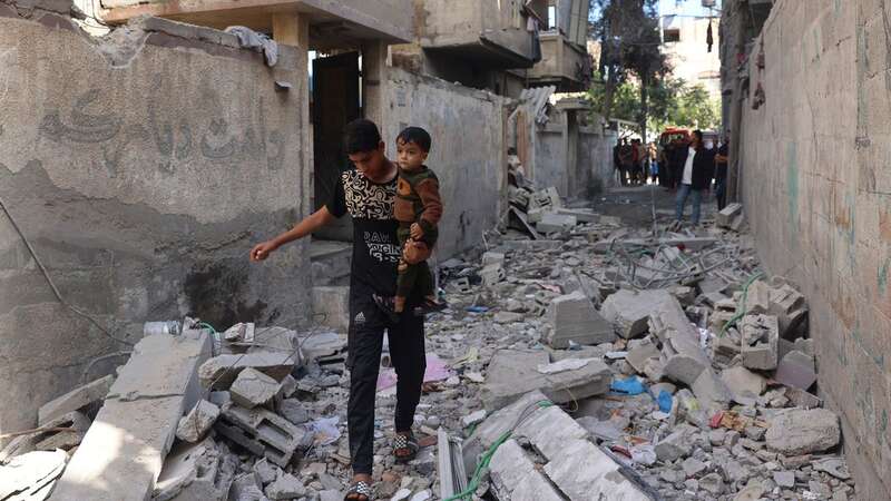 Palestinian youth carries a child as he walks through the rubble following Israeli bombardment of Rafah