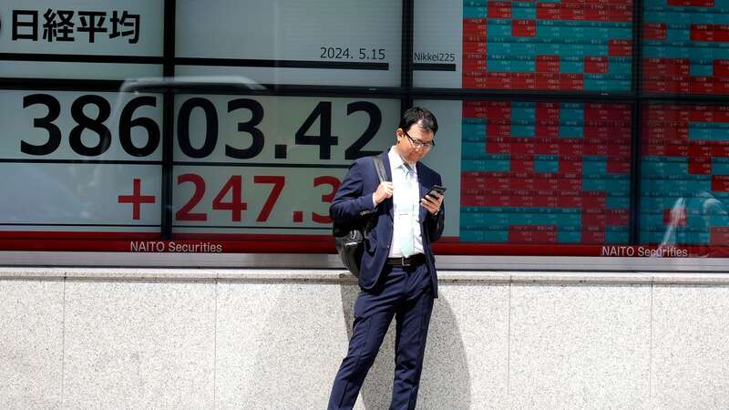 A person stands in front of an electronic stock board showing Japan