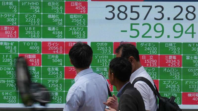 People walk in front of an electronic stock board showing Japan