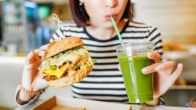 A young woman drinks green smoothies and eats a burger in a vegan fast food restaurant [file image]