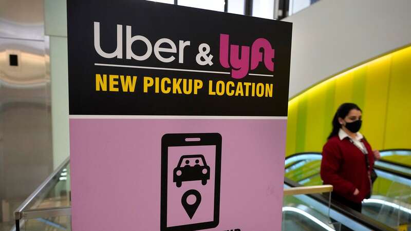 A passerby walks past a sign offering directions to an Uber and Lyft ride pickup location at an airport in Boston. Drivers for Uber and Lyft will earn a minimum pay standard of $32.50 per hour under a settlement (Image: Copyright 2021The Associated Press. All rights reserved)